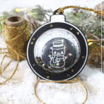 Ein Papieranhänger mit Schüttelkartenfenster. Im Fenster befindet sich ein Button und Glitzer.