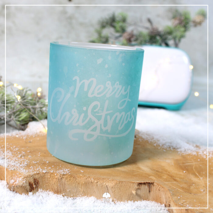 Eine satinierte / gefrostete Tasse die mit einer weihnachtlichen Banderole sublimiert wurde. Sie ist in hellblau, so dass es wie Eis aussieht. Darauf steht der Schriftzug "Merry Christmas". Im Hintergrund steht ein Cricut Joy, mit dem die Banderole erstellt wurde.