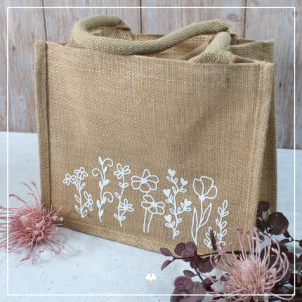 Eine Jute-Tasche mittlerer Größe, welche mit verschiedenen Blumen aus weißer Flockfolie verziert wurde.