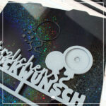 Die 32er fertige in grau gedruckte Variante der 3D Klötzchenschrift "Herzlichen Glückwunsch" - 3D Druckdatei. Sie liegt auf einer Holodruckplatte, auf welcher sich noch die Details befinden, welche in schwarz gedruckt wurden.