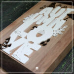 Detailaufnahme: Ein Schild aus verschiedenen Klötzchen. Die dekorativen Elemente der Lettering "Autumnlove" - Plotterdatei wurden mit dem Laser graviert. Der Schriftzug selbst ist ein 3D-Druck in weiß.