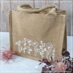 Eine Jute-Tasche mittlerer Größe, welche mit verschiedenen Blumen aus weißer Flockfolie verziert wurde.
