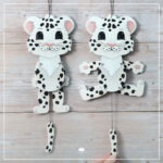 Abgebildet ist eine Hampelfigur aus Holz. Der Hampelzoo "Schneeleopard" wurde mit der Laubsäge ausgesägt und dann mit Acrylfarben bemalt. Zu sehen ist die Figur im Ruhezustand und wenn sie hampelt.