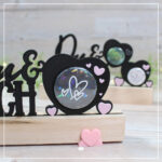 Zu sehen ist eine Nahaufnahme einer gedruckten Variante der 3D Klötzchenschrift "Du & Ich". Die Schrift wurde aus schwarzem und rosa Filament gedruckt. Die Grundfarbe ist schwarz.