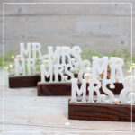 Abgebildet sind die drei Schriftvarianten der 3D Klötzchenschrift "Mr & Mrs" für unterschiedliche Buttongrößen. Sie wurden aus weißem und pfirsich-farbenem Silk-Filament gedruckt und mit dunklen Klötzchen kombiniert.