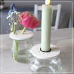 Zwei WECK-Gläser RR60 mit weißen 3D-gedruckten Blumenretter-Aufsätzen, dekoriert mit einer rosa Tulpe, blauen Perlhyazinthen und einer hellgrünen Stabkerze.