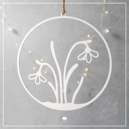 Ein weißer, 3D-gedruckter Schneeglöckchen-Kranz, filigran gedruckt, hängend an einer Jutekordel vor einem grauen Hintergrund mit stimmungsvollen, bokeh-artigen LED-Lichtern.